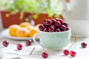 Cherries in the cup and apricots are on the table.