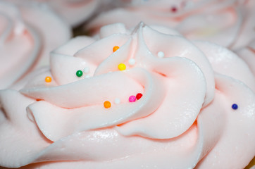 Light pink icing sprinkled with colorful candy sprinkles. Delicious sweet, smooth and creamy butter cream frosting topping for cupcakes.