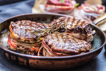 Three grilled beef tenderloin steaks coated bacon on a frying pan
