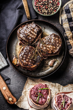 Three grilled beef tenderloin steaks coated bacon on a frying pan