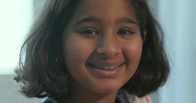 A young pretty girl of south Indian descent looks up and shows off her orthodontic braces with a big beautiful smile.