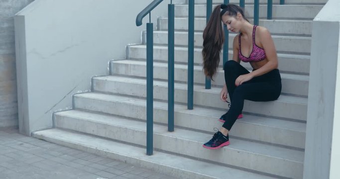 GIMBAL young woman tying shoelaces before jogging. Fitness model exercising in morning outdoors. Healthy lifestyle concept. 4K UHD