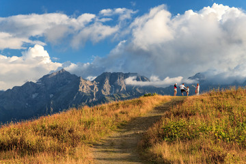 Tourists stand against Agepsta Peak in Caucasus Mountains. Beautiful scenic summer autumn landscape. Sunset blue sky scenery with clouds