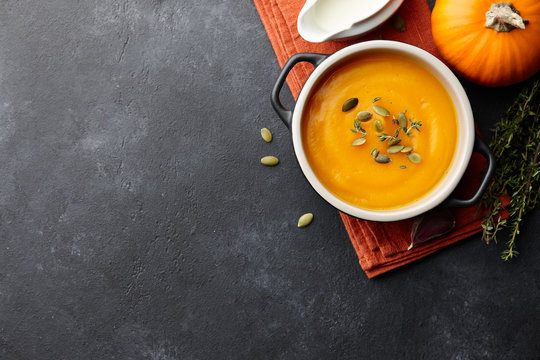 Pumpkin soup with thyme herb, cream and pumpkin seeds served in black bowl, top view