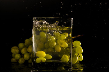 Fototapeta na wymiar a bunch of grapes on a black background. jar of water splash from falling berries