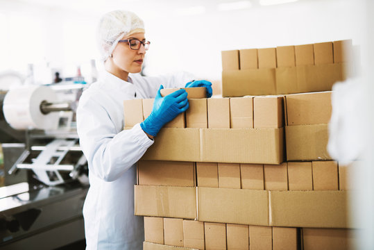 Focused female worker in sterile clothes is counting boxes ready for deliver.