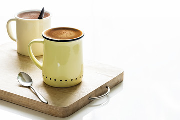 Yellow cup of coffee on wooden plate on white table