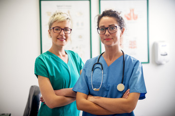Portrait of two professional nurses standing in their office in front of a camera. - obrazy, fototapety, plakaty