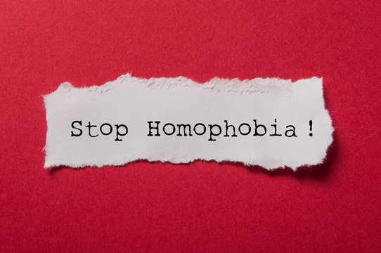 closeup of white torn paper on red paper background - Stop Homophobia !