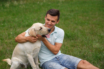 Friendship of man and dog. Happy young man is playing with his friend - dog Labrador