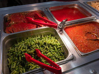 Colourful metal food serving area, red tongs, no people, fresh, clean. 