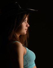 Woman standing in profile, black leather hat on her head, dark key