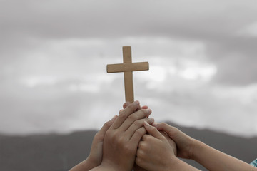 human hands praying to the GOD while holding a crucifix symbol with bright sunbeam on the sky