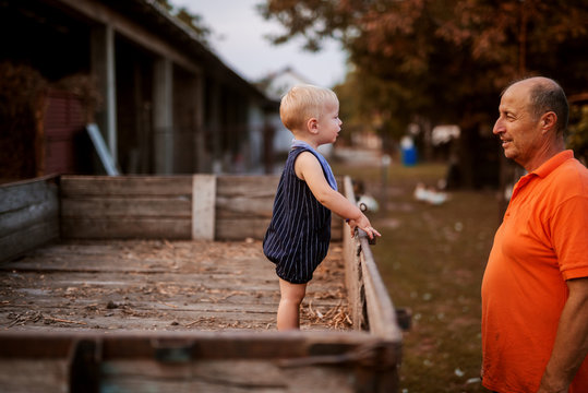 Small boy standing in a wooden trailer and looking at his grandfather. Spending some time together in a backyard alone.