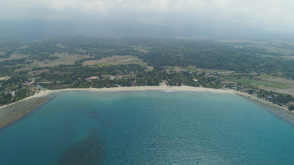 Beautiful tropical beach Cabugao with white sand and palm trees in the Philippines, Luzon. Aerial view of coast with beach and turquoise water.