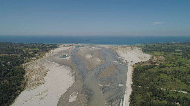 Mountain river Bucao flowing into the sea in Philippines,Luzon. Aerial view river among farmer fields flowing into the blue ocean.