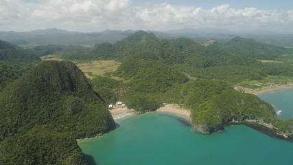 Fototapeta premium Aerial view of islands with sand beach and turquoise water in blue lagoon among coral reefs, Caramoan Islands, Philippines. Mountains covered with tropical forest.