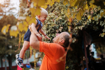 Love on first sight. Proud grandfather playing with is grandson in a backyard, lifting him in the air.