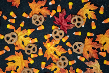 Candy corn and colorful maple leaves in an autumn scene over a black background