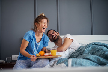 Young happy relaxed couple having breakfast together in bed. Having fun and smiling.