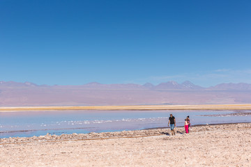 Fototapeta na wymiar Atacama, Chile - Oct 9th 2017 - Parent and a child walking on the edge of the salt flat of Atacama in a pale light, afternoon, volcano in the background, Chile.