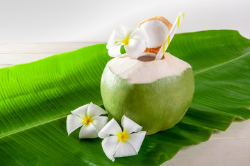 Green coconut fruit cut open to drink juice and eat. Flat lay on green banana leaf and wood background. © Chaded