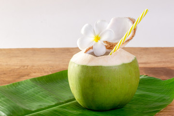 Green coconut fruit cut open to drink juice and eat. Flat lay on green banana leaf and wood background. © Chaded