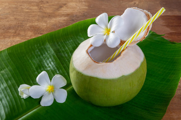 Green coconut fruit cut open to drink juice and eat. Flat lay on green banana leaf and wood background. © Chaded