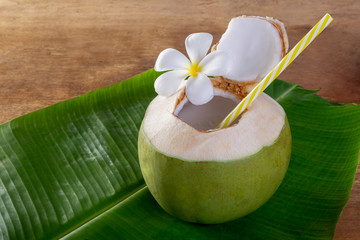 Green coconut fruit cut open to drink juice and eat. Flat lay on green banana leaf and wood background. © Chaded