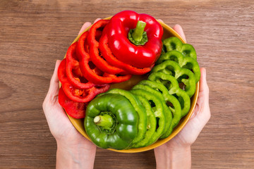 Hand holding slices of red bell pepper and green bell pepper on wood background