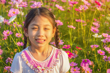 The little girl in the field of pink cosmos flower (Cosmos Bipinnatus) at sunlight in the morning