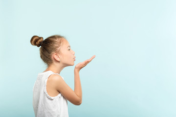 cute girl blowing a kiss. pretty young child sending love. romance and warm feelings concept. portrait on blue background.