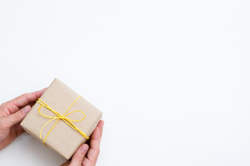 holiday presents wrapped in craft paper and tied with a yellow twine. hand offering a simple reward on festive holiday. package on white background with copy space.