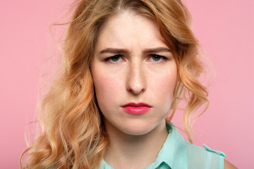 Naklejka premium serious young woman with a troubled look and gathered brows. emotion and feelings concept. portrait of alarmed worried concerned girl on pink background.