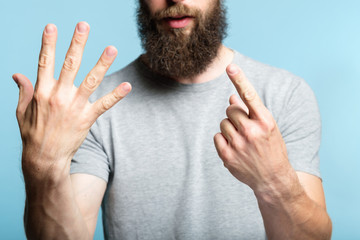 bearded man showing number six with his hand. cropped shot of a male torso on blue background....