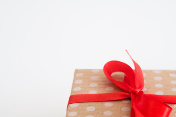 christmas present in gift box wrapped in craft dotted paper and tied with a red ribbon bow. festive package on white background with free space.