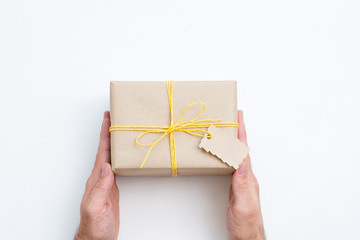 handmade craft present. hands holding gift wrapped in paper and tied with yellow twine. festive package on white background.