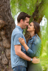 Fototapeta premium Young attractive happy couple smiling and looking at each other under a tree