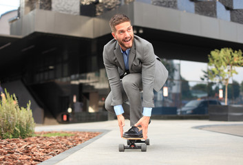 Confident young businessman in business suit on longboard hurrying to his office, on the street in...