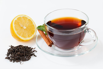 A glass cup with black tea on a saucer with mint, cinnamon, as well as tea leaves and lemon