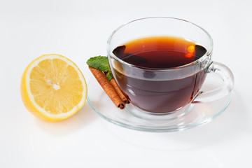 A glass cup with black tea on a saucer with mint, cinnamon, as well as lemon