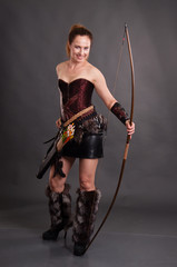 Woman in an amazon suit with a bow on a dark background. The girl shoots from an onion