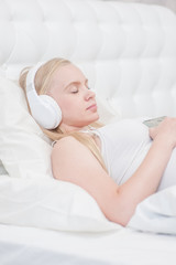 pregnant woman lying on bed at home and listening music in headphones