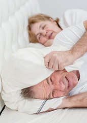 Angry senior man covered his ears with a pillow so as not to hear the snoring of his wife