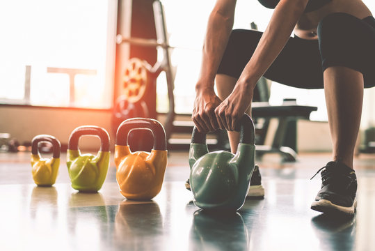 Close up of woman lifting kettlebell like dumbbells in fitness sport club gym training center with sport equipment near window background. Lifestyles and workout exercise for bodybuilding and healthy