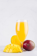 Tropical summer juice of ripe fresh mango with pulpy chopped slice on soft light elegant white background, vertical.