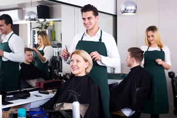 Professional stylist cutting hair of elderly blonde