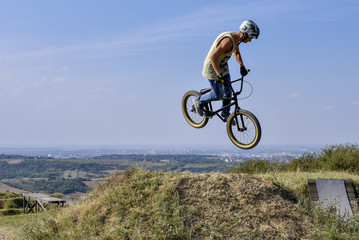 Naklejka na ściany i meble Man in helmet on bmx bike jumping and flying on the hill