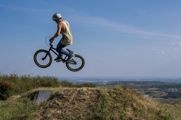 Young man on bmx bike jumping and flying on the hill