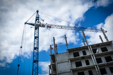 Construction crane in front of a building against a sky with clouds